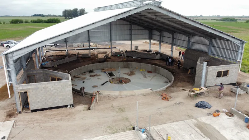 Vista aérea de la sala de ordeñe en obra: la platea circular de la rotativa de 60 posiciones dentro del galpón, con los muros de bloques a medio levantar