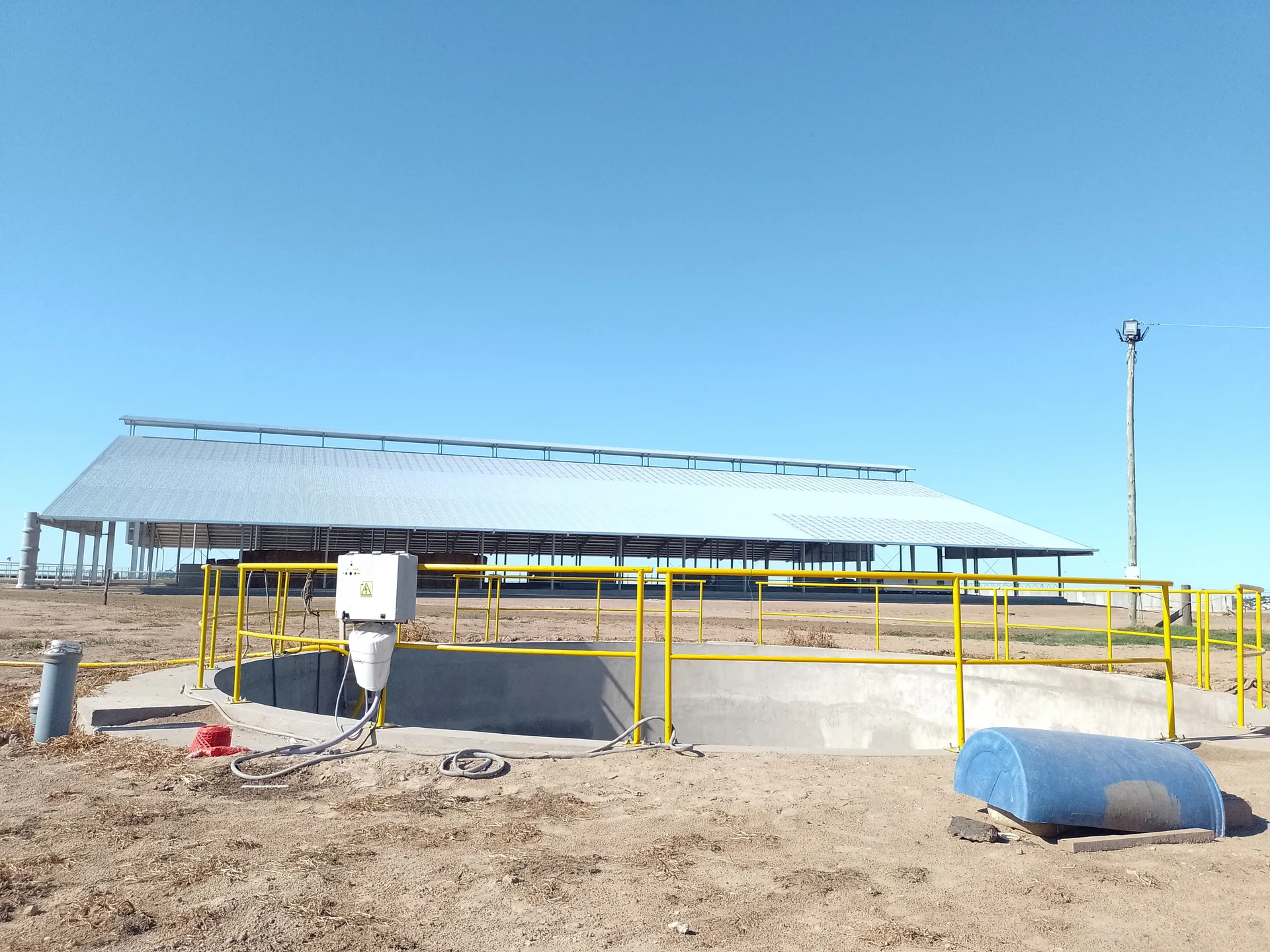 Corral de vivienda terminado, con cubierta metálica a dos aguas sobre estructura abierta y la pileta de efluentes de hormigón en primer plano