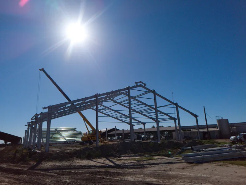 Montaje de la estructura metálica del galpón con grúa, a contraluz contra el cielo despejado
